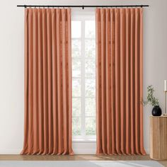 an orange curtain hanging in front of a window with white walls and wooden flooring