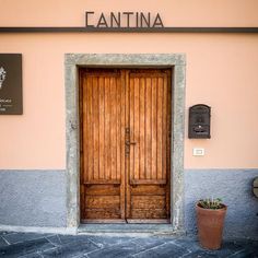 two wooden doors are open in front of a pink and gray building with a planter