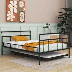 a black metal bed frame in a room with wood floors and pink walls, along with potted plants