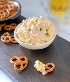 a bowl of chicken salad with pretzels on the side and a glass of beer