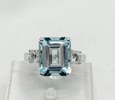 an aquamarinee and diamond ring is displayed on a clear glass display case with white background