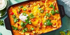 an enchilada casserole with sour cream and cilantro on the side