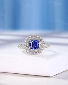 a blue and white diamond ring sitting on top of a white box with diamonds around it