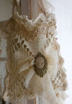 an old fashioned clock is hanging from a curtain with lace and ribbon on it's side