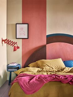 a bed sitting in front of a wall with pink and brown sheets on top of it