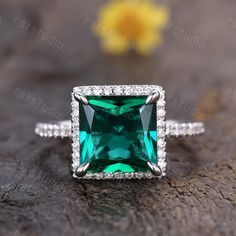 an emerald colored stone surrounded by diamonds on top of a piece of wood with flowers in the background