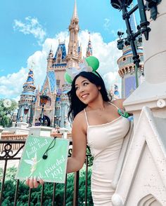 a woman in a white dress standing next to a fence with a castle behind her