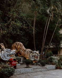 two large tiger statues sitting on top of a stone walkway next to trees and bushes