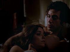 a man and woman laying in bed with one holding the other's arm around her