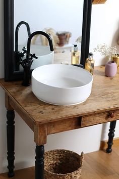 a white bowl sink sitting on top of a wooden table next to a black faucet