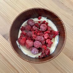 a wooden bowl filled with yogurt and raspberries