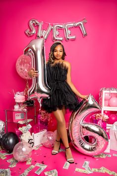 a woman standing in front of a pink backdrop with balloons and streamers