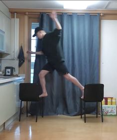 a man jumping in the air with his feet up on two chairs and a curtain behind him