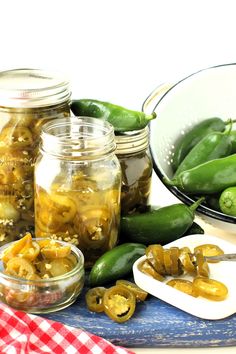 pickled green peppers in jars and spoons on a cutting board next to other vegetables