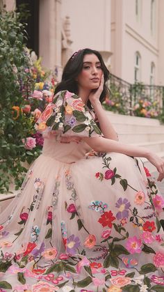 a woman in a floral dress sitting on steps with her hand under her chin and looking off to the side