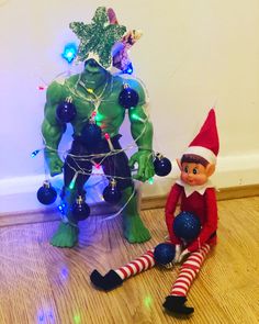 an elf sitting next to a christmas tree with lights on it and a green man dressed as the grin