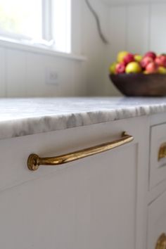 a bowl of fruit sitting on top of a white countertop next to a window