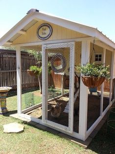 a small white shed sitting in the middle of a yard with potted plants on it