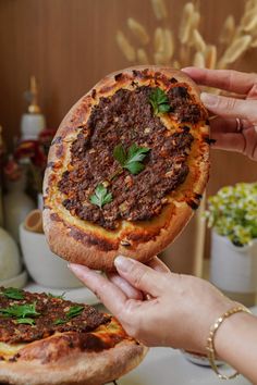 two people holding up pizzas with meat and herbs on them