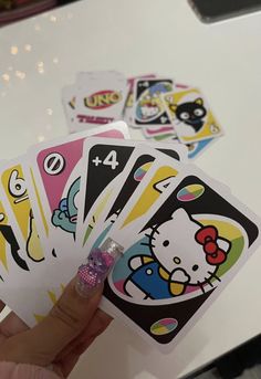 a hand holding four hello kitty playing cards on a table with people in the background