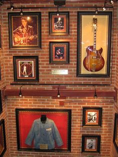 a room filled with framed pictures and guitars on the wall next to a red brick wall