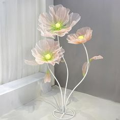 three pink flowers in a white vase on a table next to a window sill