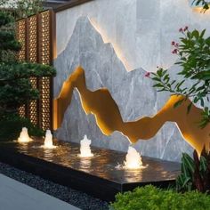 an outdoor fountain with lights in front of a wall and trees on the other side