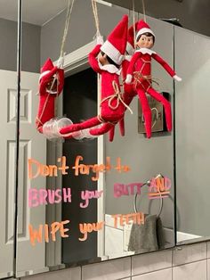 two elfs hanging from a mirror with words written on the wall above them that read, don't forget to brush your teeth wipe your teeth