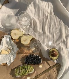 an assortment of fruits and cheeses on a paper bag with water glasses, spoons and other items