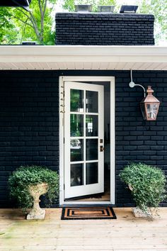 a black brick house with two potted plants on the front porch and an open door