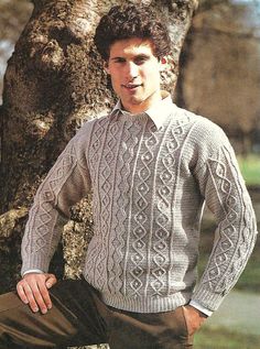 a man standing next to a tree wearing a sweater