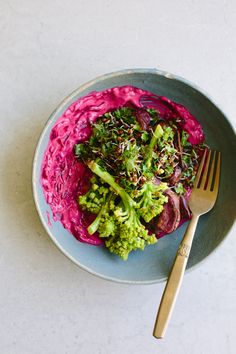 a blue bowl filled with broccoli and beet slaw next to a fork