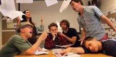 a group of people sitting around a table with papers flying in the air over them