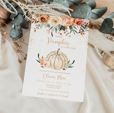 a white and gold pumpkin baby shower is displayed on a table with greenery, leaves and flowers