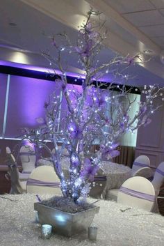 the centerpiece is decorated with purple lights and branches in a silver vase on top of a table