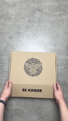 someone holding up a box with the words be kinder on it in front of a concrete background