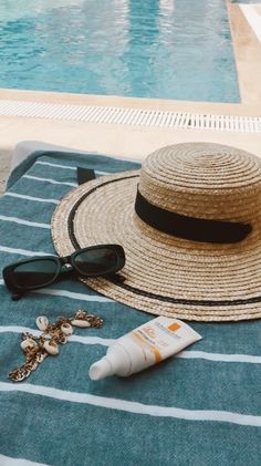 a hat, sunglasses and sunscreen on a towel next to a pool