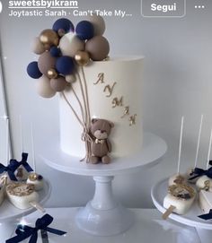 a white cake with blue and gold balloons on it's top is surrounded by other desserts