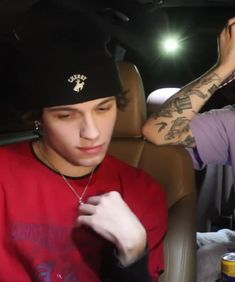 two young men sitting in the back seat of a car, one with tattoos on his arm