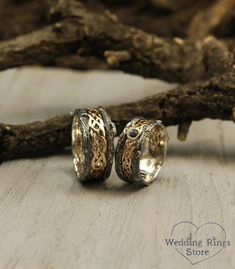 two wedding rings sitting next to each other on top of a wooden table with branches in the background