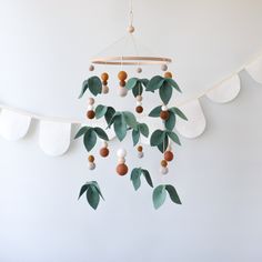 a mobile with leaves and balls hanging from it's sides on a string in front of a white wall