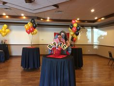 a man sitting on top of a red chair in front of a table with balloons