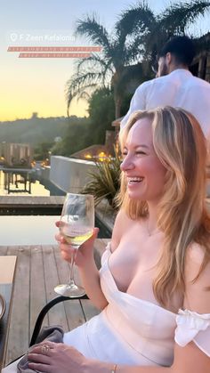 a woman sitting at a table with a glass of wine in her hand and smiling