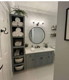 a bathroom with gray cabinets and white towels on the shelves, along with a round mirror