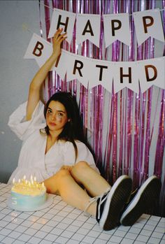 a woman sitting in front of a birthday cake with candles on it and the words happy birthday hanging above her