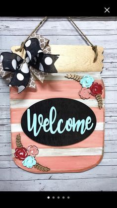 a welcome sign hanging on the side of a wooden wall with polka dots and flowers