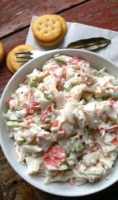 a white bowl filled with chicken salad next to crackers and a fork on the side