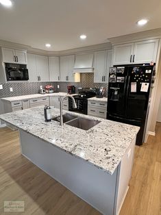 a kitchen with white cabinets and granite counter tops, black appliances and stainless steel sink