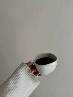 a person holding a cup of coffee in their left hand, against a white wall