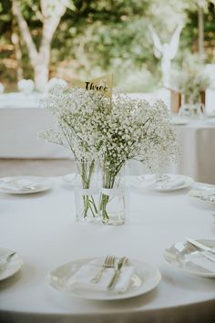 two vases filled with baby's breath flowers on top of a white table cloth